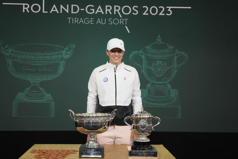 Defending champion Poland's Iga Swiatek poses by the men's trophy, left, and the women's trophy during the French Open tennis tournament draw at the Roland Garros Stadium, Thursday, May 25, 2023 in Paris. Play begins at the French Open on Sunday, May 28, 2023 and runs until Sunday June 11, 2023. (AP Photo/Thibault Camus)