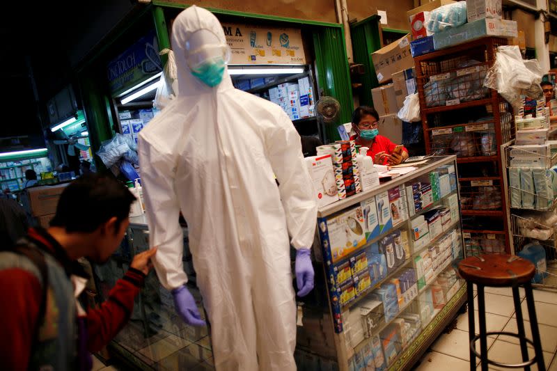 FILE PHOTO: A vendor wearing a mask waits for customers while a man looks at a protective suit displayed for sale at whole-sale market for medical stuffs, following the outbreak of the new coronavirus in China, in Jakarta