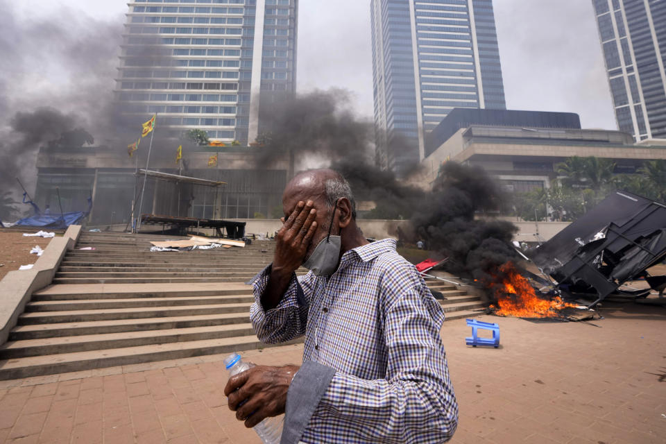 A Sri Lankan man reacts to tear gas as he walks past the vandalized site of anti-government protests outside president's office in Colombo, Sri Lanka, Monday, May 9, 2022. Authorities deployed armed troops in the capital Colombo on Monday hours after government supporters attacked protesters who have been camped outside the offices of the country's president and prime minster, as trade unions began a “Week of Protests” demanding the government change and its president to step down over the country’s worst economic crisis in memory. (AP Photo/Eranga Jayawardena)