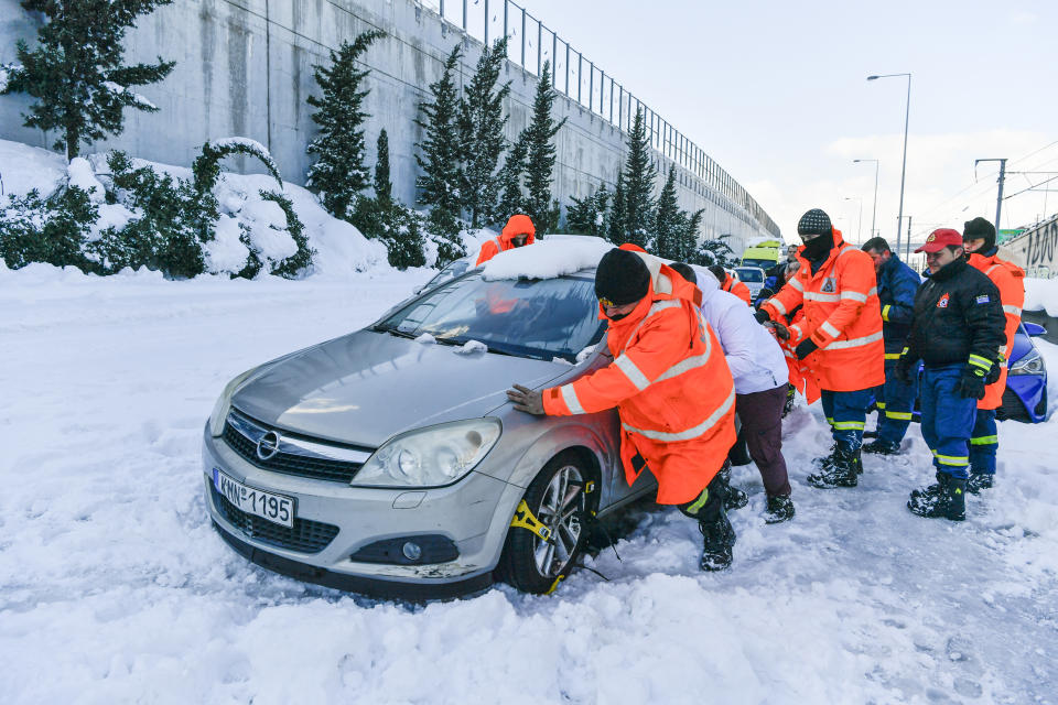 Firemen push a trapped vehicle at a motorway, after a snowstorm, in Athens, on Tuesday, Jan. 25, 2022. Rescue crews in Istanbul and Athens scrambled on Tuesday to clear roads that came to a standstill after a massive cold front and snowstorms hit much of Turkey and Greece, leaving countless people and vehicles in both cities stranded overnight in freezing conditions. (AP Photo/Michael Varaklas)