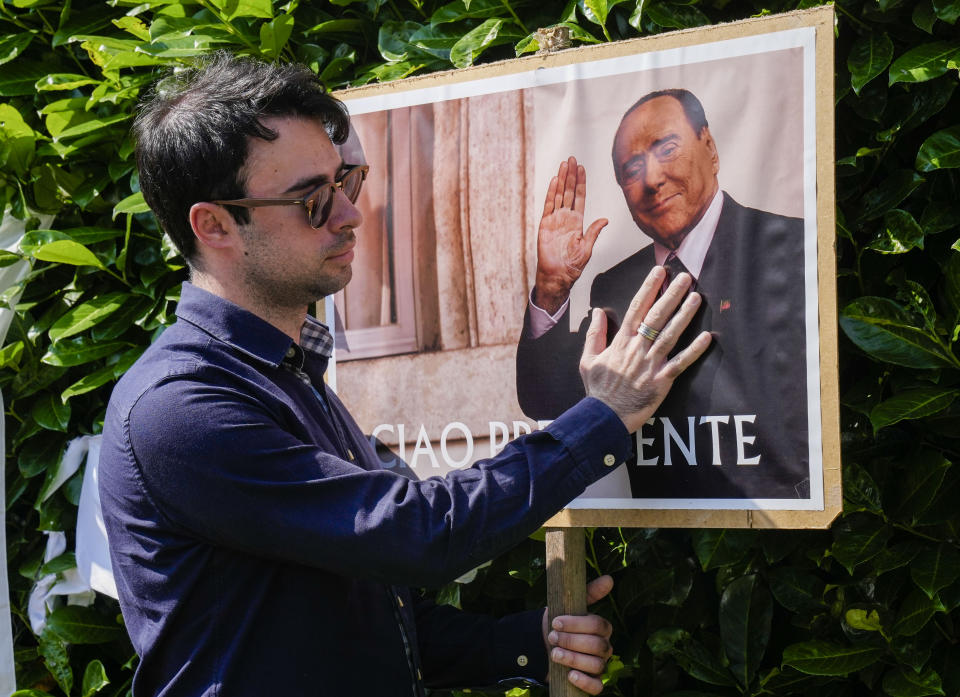 Un hombre se detiene frente a un cartel con la imagen de Silvio Berlusconi en las afueras de la residencia del fallecido ex primer ministro, en Arcore, cerca de Milán, el lunes 12 de junio de 2023. (AP Foto/Antonio Calanni)