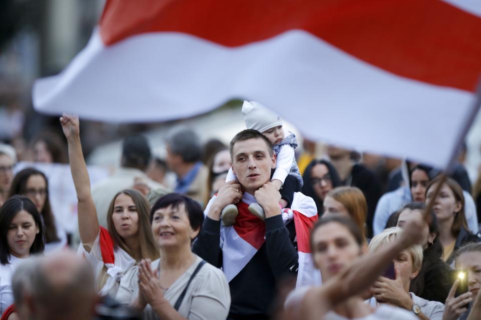 Belarusian opposition supporters with an old Belarusian national flag gather in the rain at Independence Square in Minsk, Belarus, Wednesday, Aug. 26, 2020. Protests demanding the resignation of Belarus' authoritarian President Alexander Lukashenko have entered their 18th straight day on Wednesday. (AP Photo/Sergei Grits)