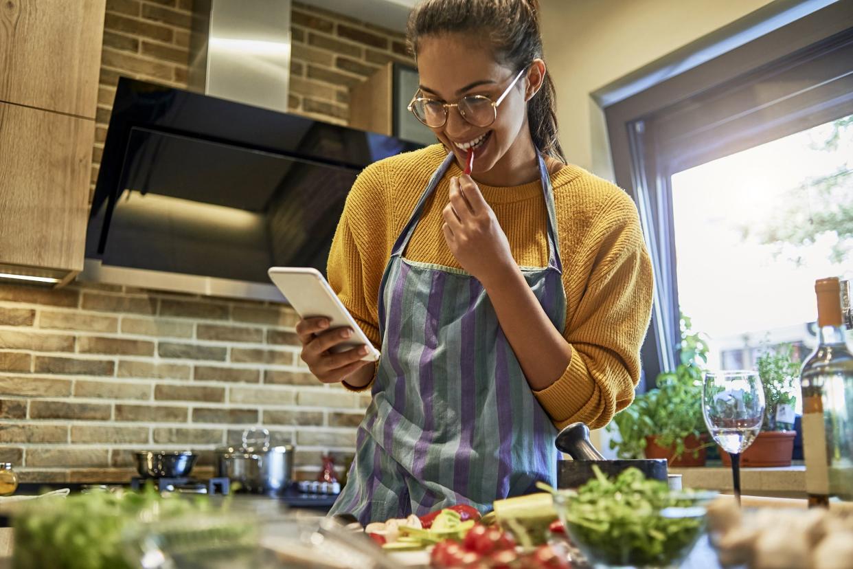 young woman consulting smartphone for recipe while cooking in kitchen