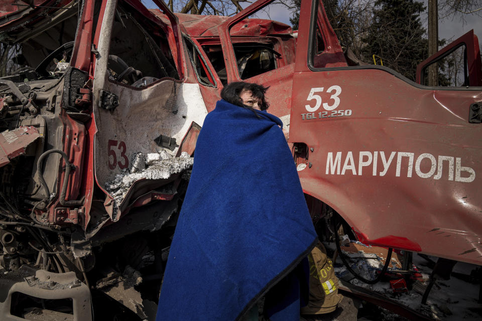A woman covers herself with a blanket near a damaged fire truck after shelling in Mariupol, Ukraine, Thursday, March 10, 2022. (AP Photo/Evgeniy Maloletka)