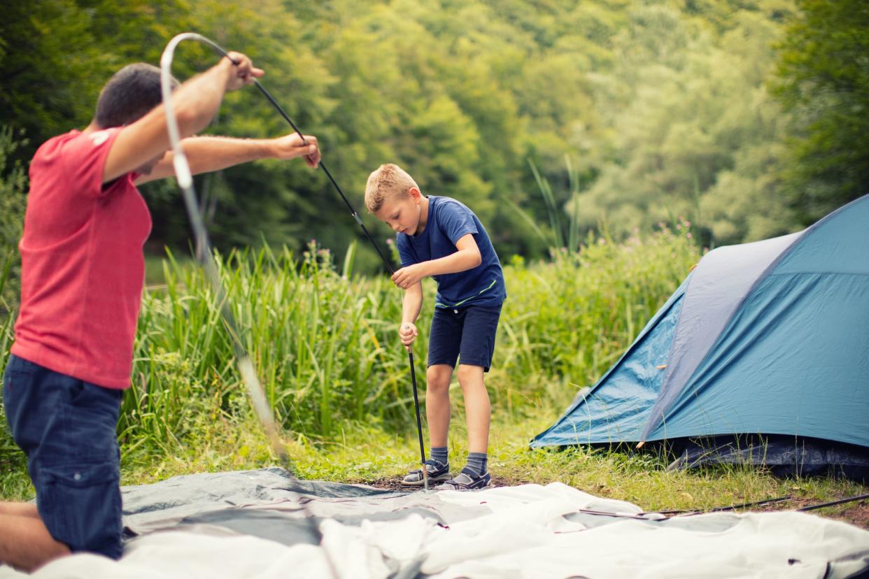 Boy setting tent with his father at camping in wonderful nature.
