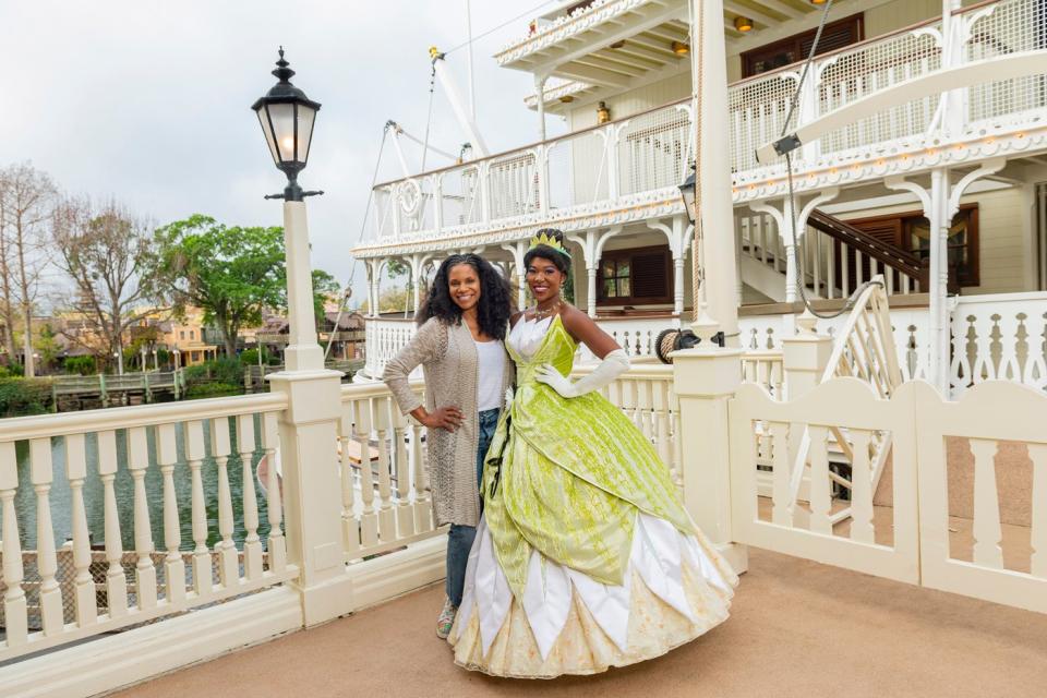 Tiana greeting a theme park guest near a river boat.