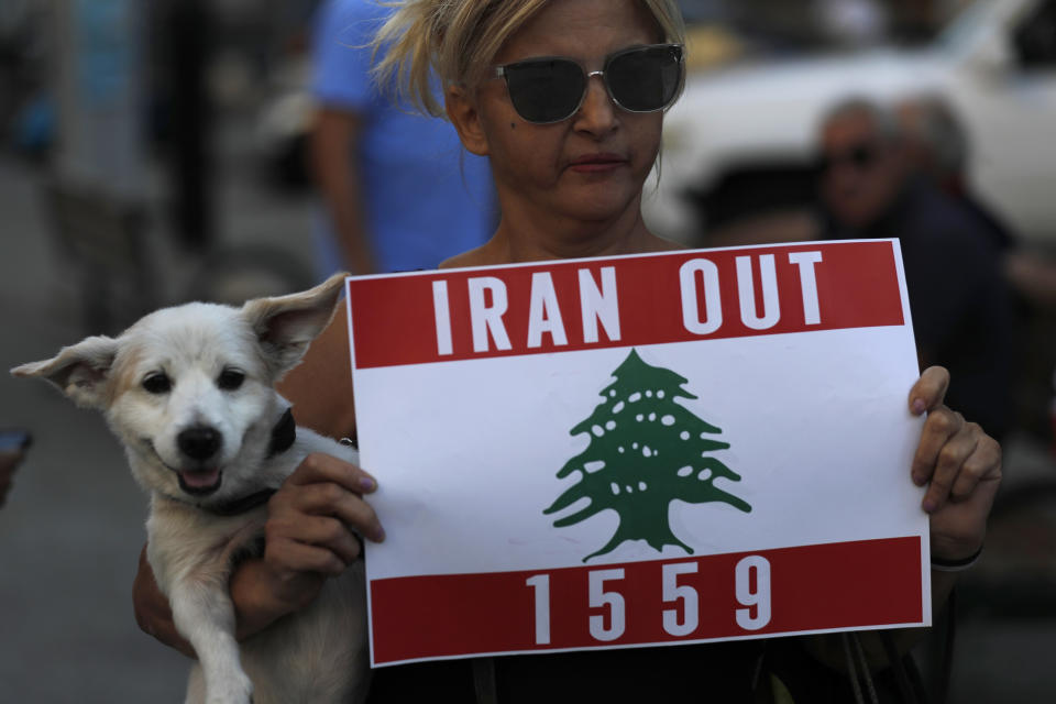 A Lebanese protester carries her dog and holds a placard during a protest against the Hezbollah group and the visit of the Iranian Foreign Minister Hossein Amirabdollahian who will meet with Lebanese officials on Thursday, in Beirut, Lebanon, Wednesday, Oct. 6, 2021. (AP Photo/Hussein Malla)