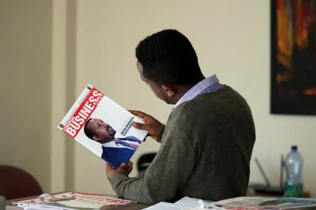 Eritrean refugee Berhane reads news magazine with cover photo of Ethiopian PM at his office in Addis Ababa