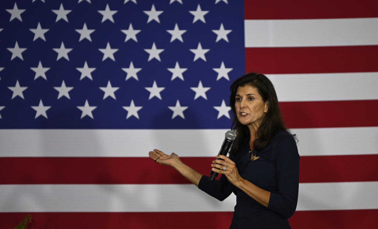 Nikki Haley holds a microphone in front of an American flag.