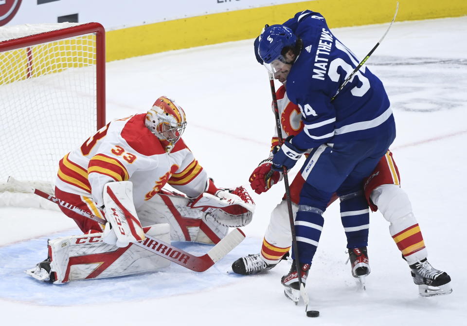 Toronto Maple Leafs centre Auston Matthews (34) gets tied up by Calgary Flames defenceman Mark Giordano (5) as Flames goaltender David Rittich (33) keeps a close eye on the loose puck during third period NHL hockey action in Toronto on Monday, Feb. 22, 2021. (Nathan Denette/The Canadian Press via AP)