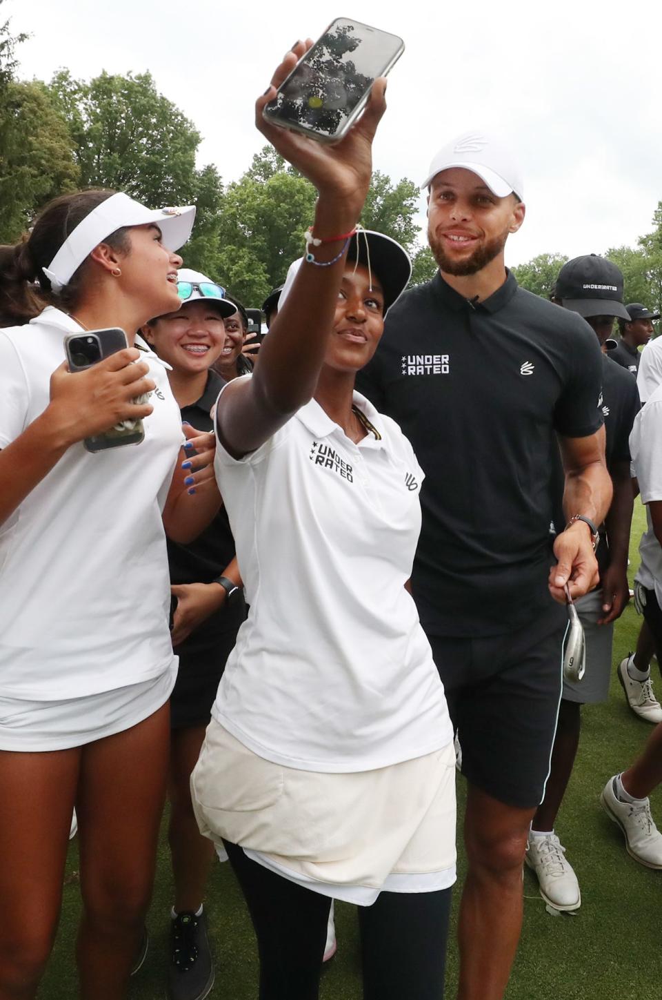 A player on the Underrated Golf tour takes a selfie with Stephen Curry as they walk on the South Course at Firestone Country Club in Akron.