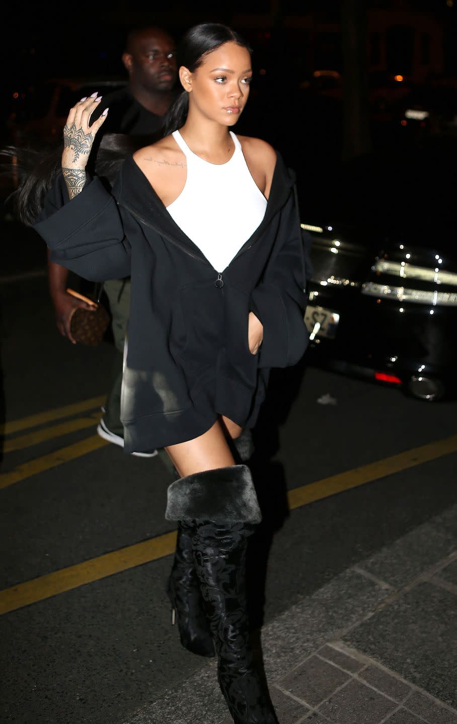 <p>In a racer-front white mini dress, with an oversized zip-up hoodie and thigh-high fur boots.</p>