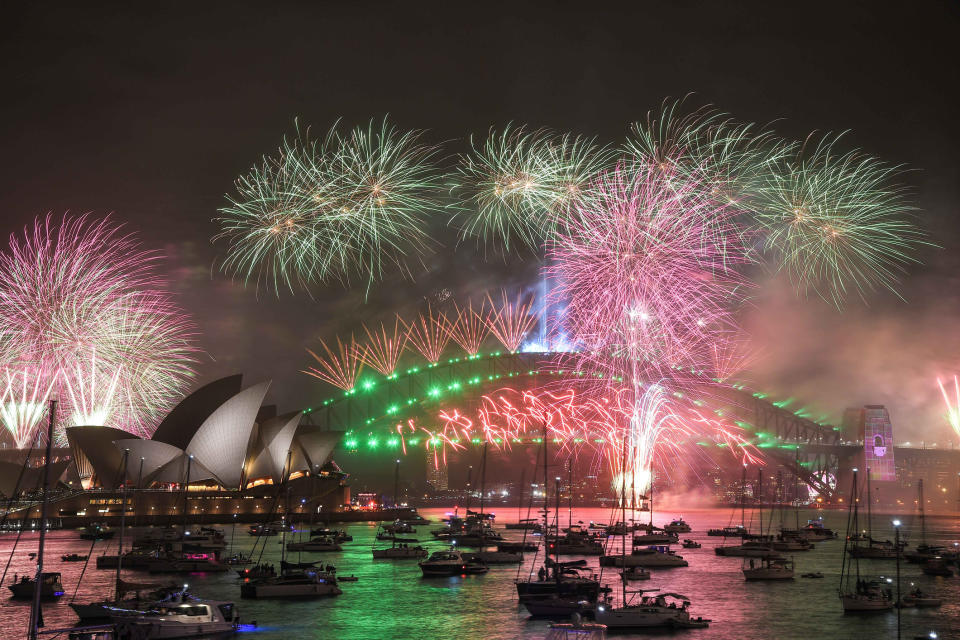 Sydney Opera House and Harbour Bridge with vibrant fireworks display during a nighttime celebration. Boats are in the water below the fireworks