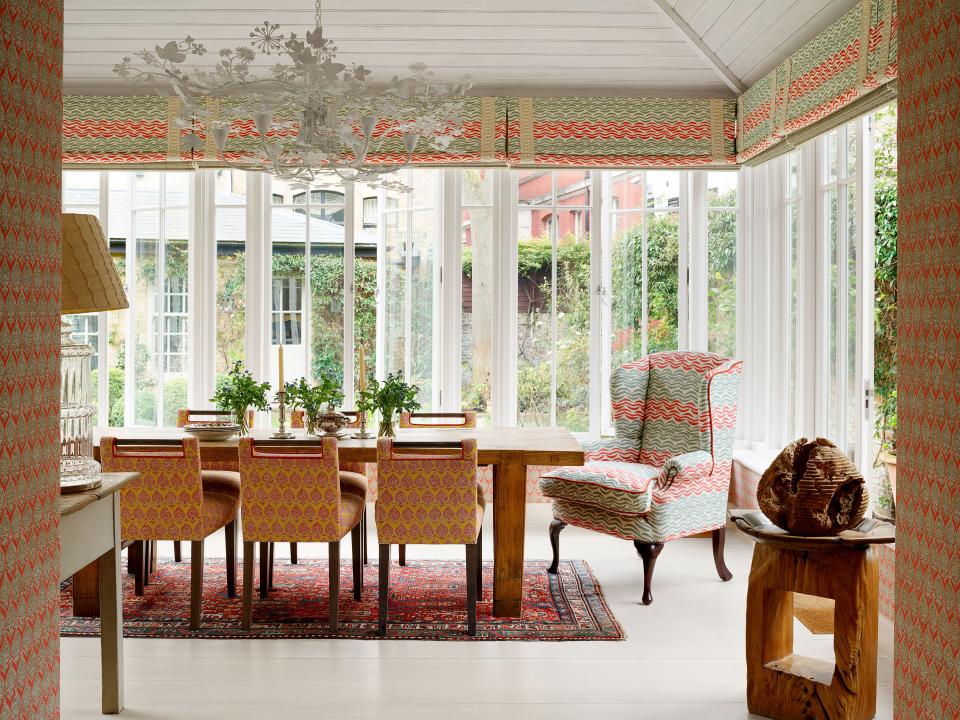 In the dining room, an armchair and the pelmets are made of the same Raoul Textiles linen. A Tord Boontje chandelier hangs about the oak dining table with chairs by Kit Kemp; antique Turkish rug.