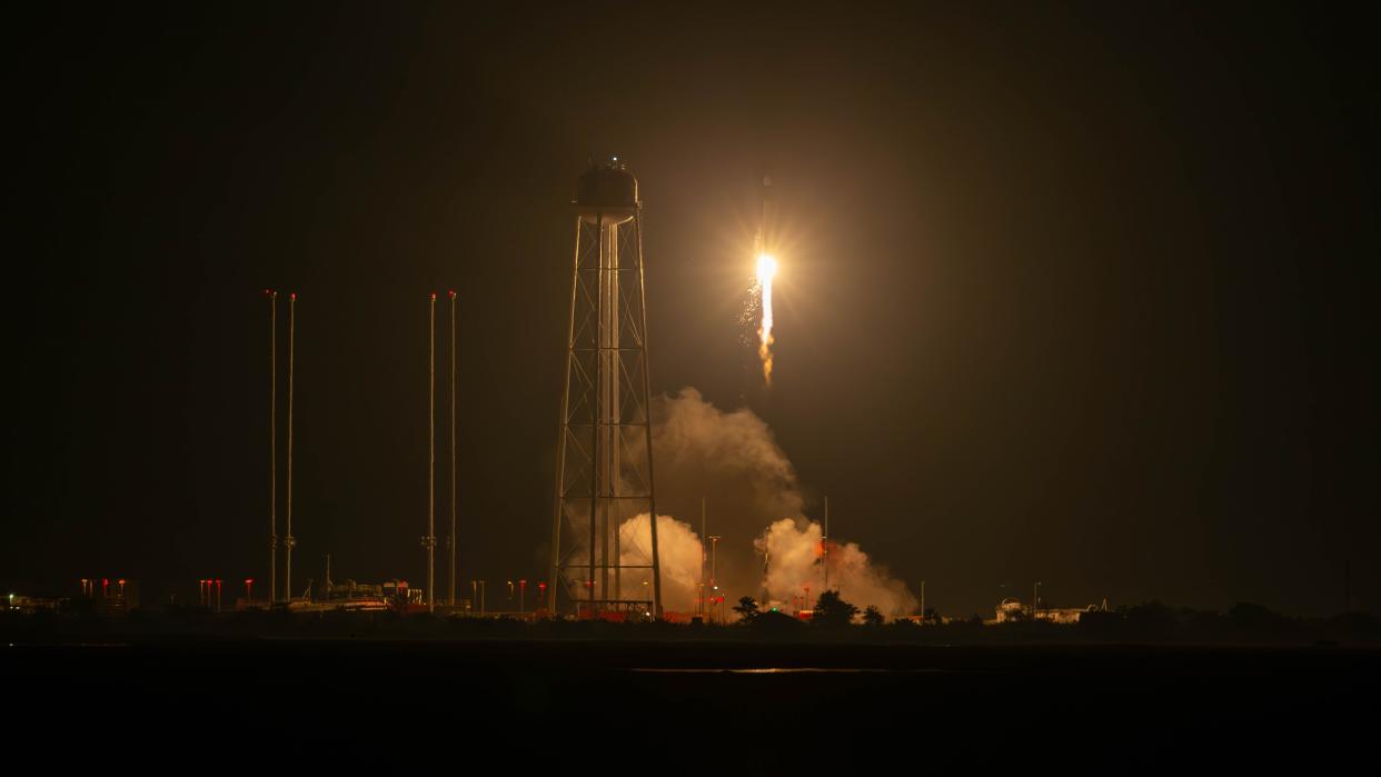  Rocket launch at night shows a bright lights and billowing plume below as the rocket lifts off from the launch pad. 