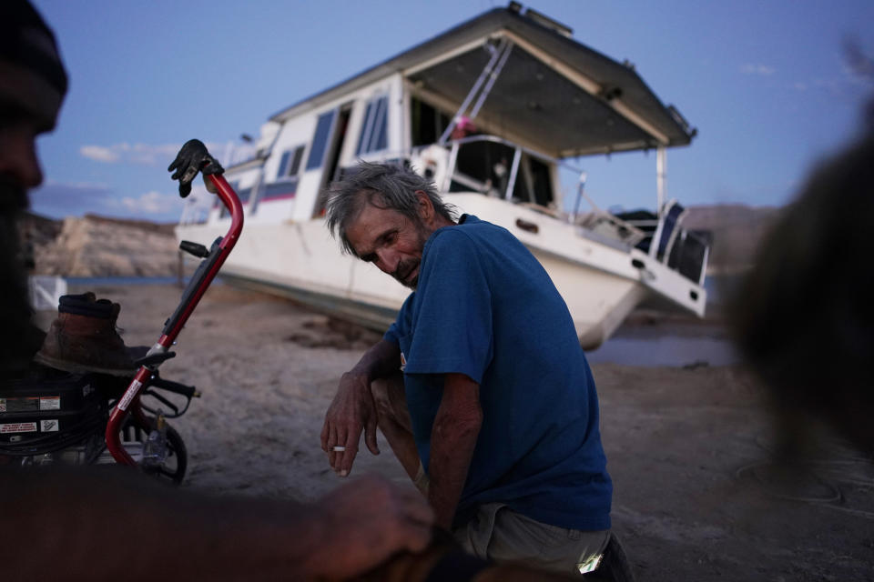 Craig Miller smokes a cigarette beside his stranded houseboat at the Lake Mead National Recreation Area, Thursday, June 23, 2022, near Boulder City, Nev. Miller had been living on the stranded boat for over two weeks after engine trouble and falling lake levels left the boat above the water level. (AP Photo/John Locher)