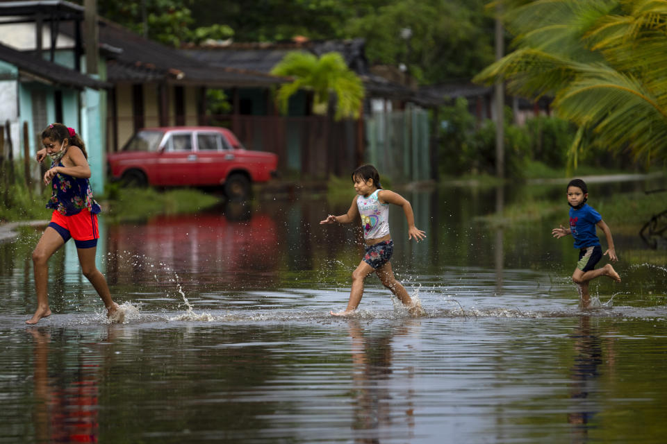 Children run in a flooded street caused by rains brought on by Hurricane Ida, in Guanimar, Artemisa province, Cuba, Saturday Aug. 28, 2021. (AP Photo/Ramon Espinosa)