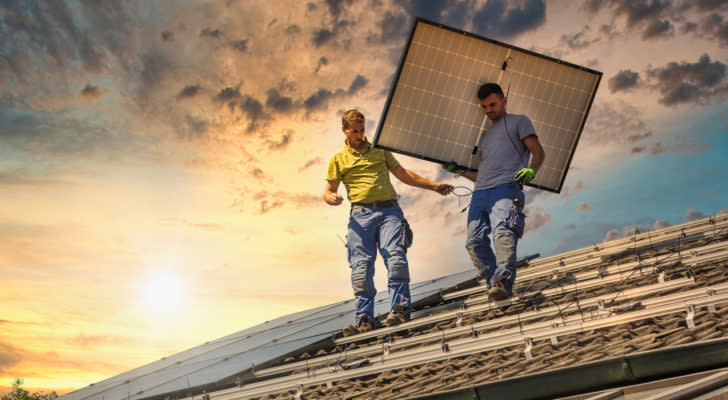 A photo of two men installing a solar panel. Solar stocks