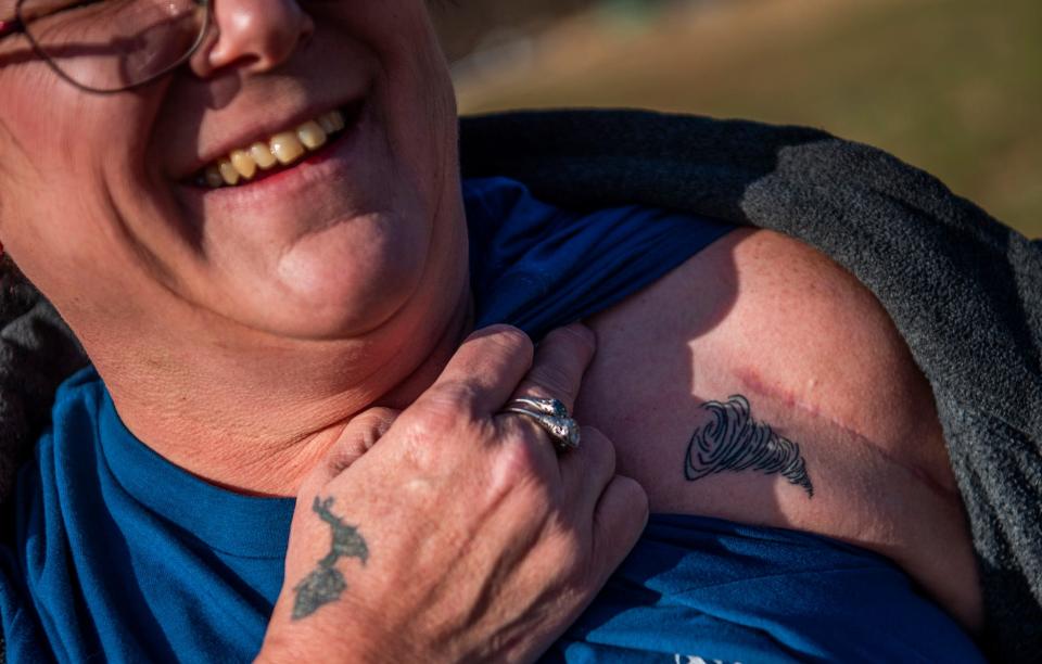 Standing where she may have been blown across West Wolf Mountain Road, Felene Taylor shows the tornado tattoo she got near the scar from her shoulder surgery she needed after the tornado on Friday, March 30, 2023.