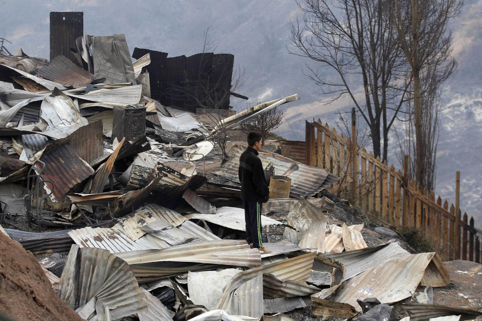 A man stands over and looks at the charred remains of homes after a large forest fire reached urban areas in Valparaiso, Chile, Sunday April 13, 2014. Authorities say the fires have destroyed hundreds of homes, forced the evacuation of thousands and claimed the lives of at least seven people. ( AP Photo/ Luis Hidalgo)