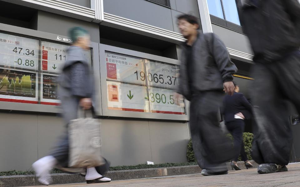 People walk past an electronic stock indicator of a securities firm in Tokyo, Wednesday, March 22, 2017. Shares fell in Asia early Wednesday after U.S. stocks took their biggest loss in five months. The sell-off overnight on Wall Street was spurred by obstacles to a health care bill backed by U.S. President Donald Trump that also raised questions over prospects for his agenda of boosting growth by cutting taxes and regulations. (AP Photo/Shizuo Kambayashi)