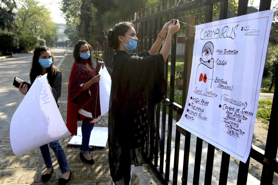 Christian volunteers fix a placard regarding the symptoms for the new coronavirus on a street for awareness, in Peshawar, Pakistan Sunday, March 15, 2020. For most people, the new coronavirus causes only mild or moderate symptoms. For some, it can cause more severe illness, especially in older adults and people with existing health problems. (AP Photo/Mohammad Sajjad)