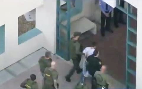 Police escort a suspect into the Broward Jail after checking him at the hospital following a shooting incident at Marjory Stoneman Douglas High School in Parkland - Credit: Reuters