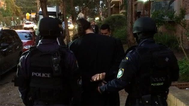 Heavily armed officers lead away an 18-year-old man arrested at Wentworthville following Wednesday morning's raids. Photo: NSW Police