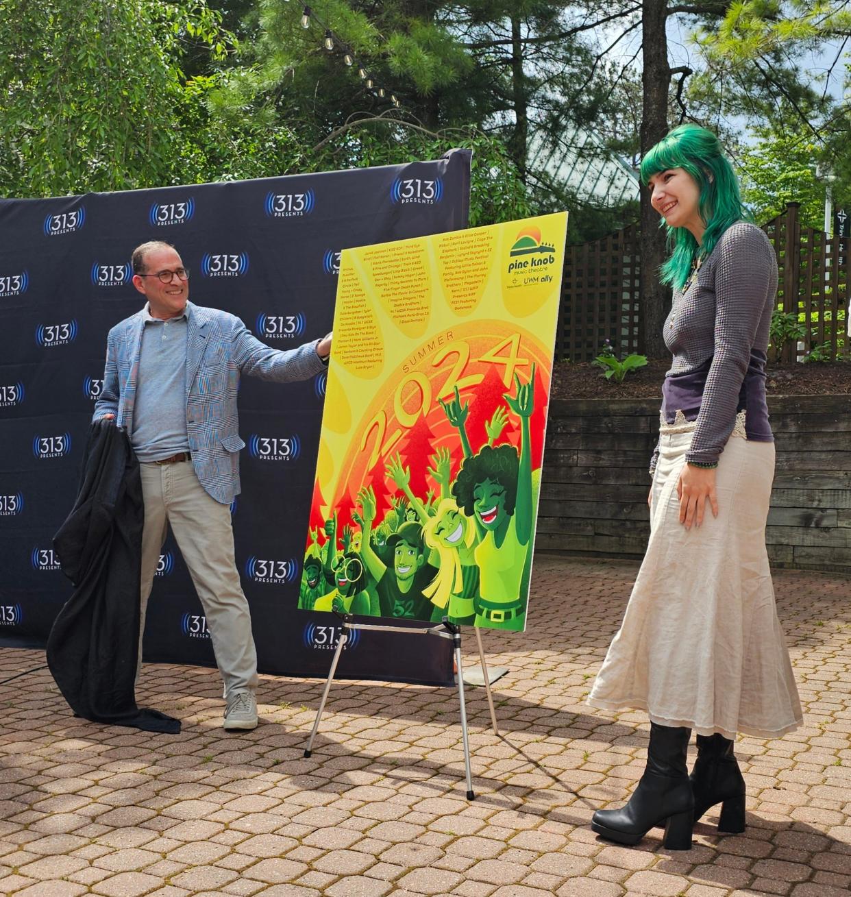 313 Presents President Howard Handler, left, unveils the winning 2024 Pine Knob poster design by College for Creative Studies student Kat Sutherland, right.