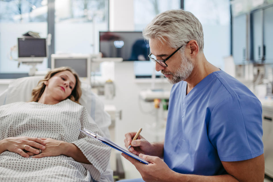 Healthcare professional taking notes next to a patient lying on a hospital bed