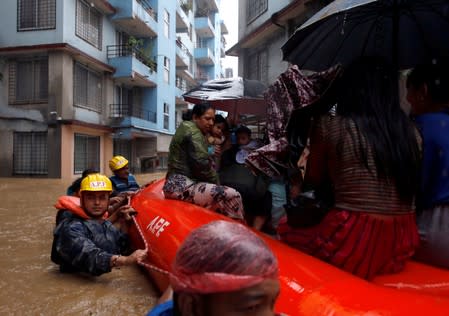 A woman carrying a child is moved by rescue workers towards dry ground from a flooded colony in Kathmandu