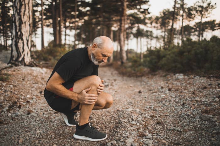 A man rubbing his knee on a running trail