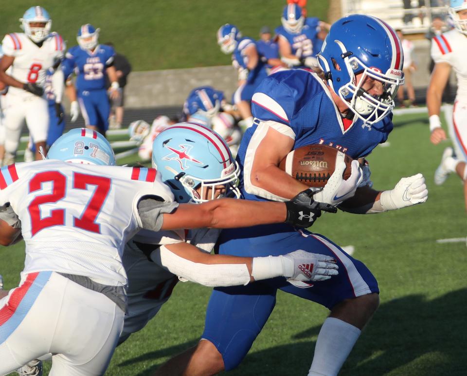 Lake's Nathan Baker runs as Alliance's Brady White, left, and Logan McCreedy, center, try to make the tackle, Friday, Aug. 18, 2023.