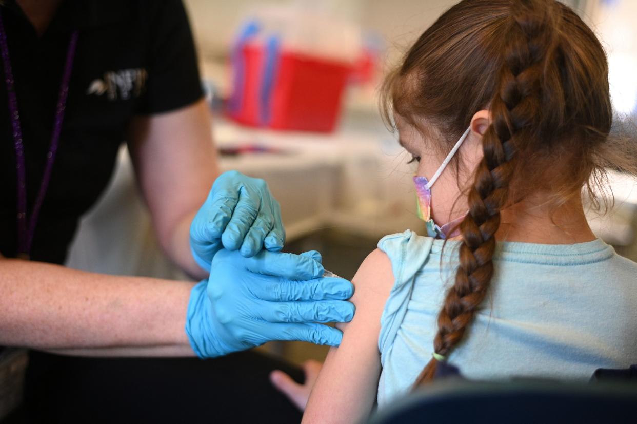 A nurse administers a pediatric dose of the COVID-19 vaccine to a girl at a vaccination clinic.