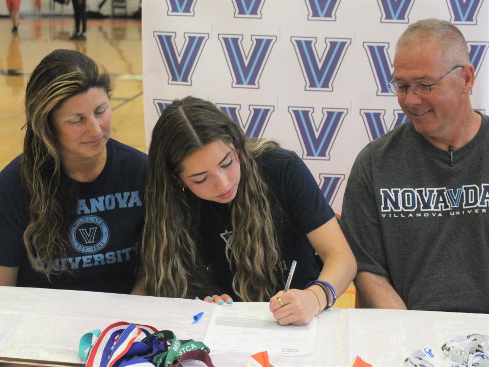 Crystal O'Leary (left) and Brian O'Leary (right) watch on as their daughter Caelen O'Leary (center) signs her National Letter of Intent committing to Villanova University in a ceremony at Taunton High School.