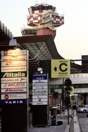 In a vertical frame, signage for airlines and Terminal C stack up with an air traffic control-tower protruding behind.