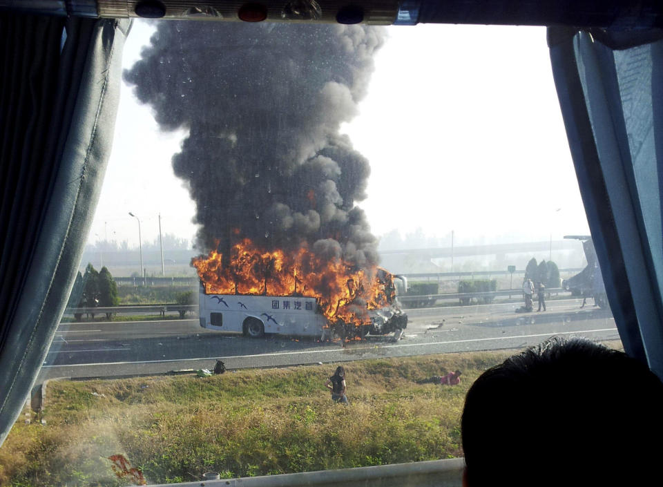 In this photo taken with a cell phone through a glass window of another vehicle and distributed by China's Xinhua News Agency, a tourist bus is engulfed in flames on an expressway near Tianjin, China, Monday, Oct. 1, 2012. Five Germans and a Chinese citizen were killed when the bus burst into flames after hitting the back of a truck, Xinhua said. (AP Photo/Xinhua) NO SALES