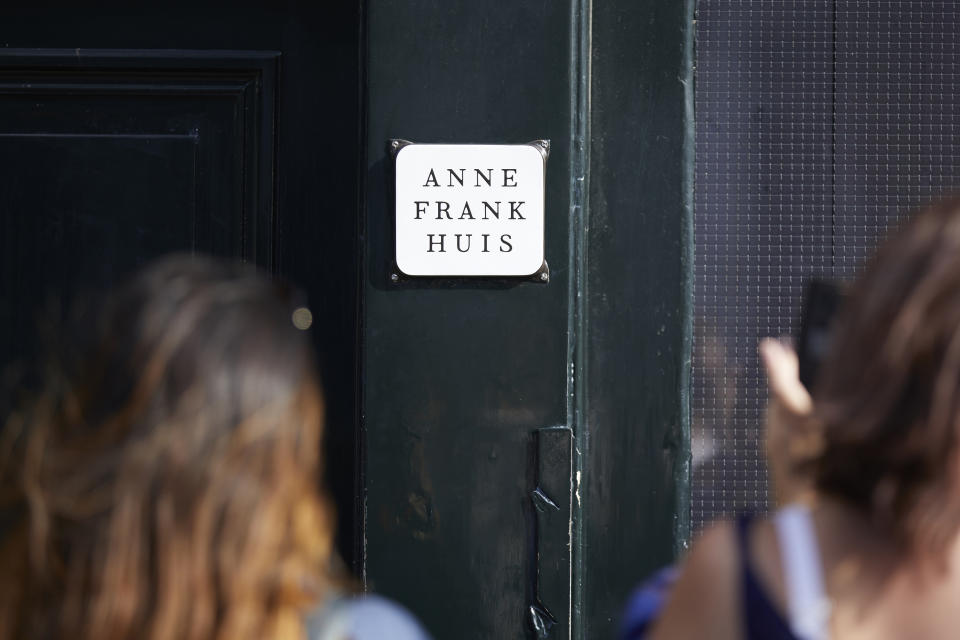 People standing outside a building that has a plaque with the words "Anne Frank Huis" on it