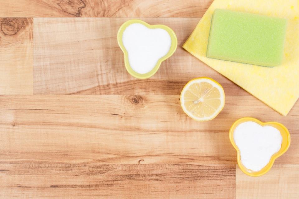 Small bowls of salt, a slice of lemon, and a cleaning rag and sponge on a wooden cutting board.