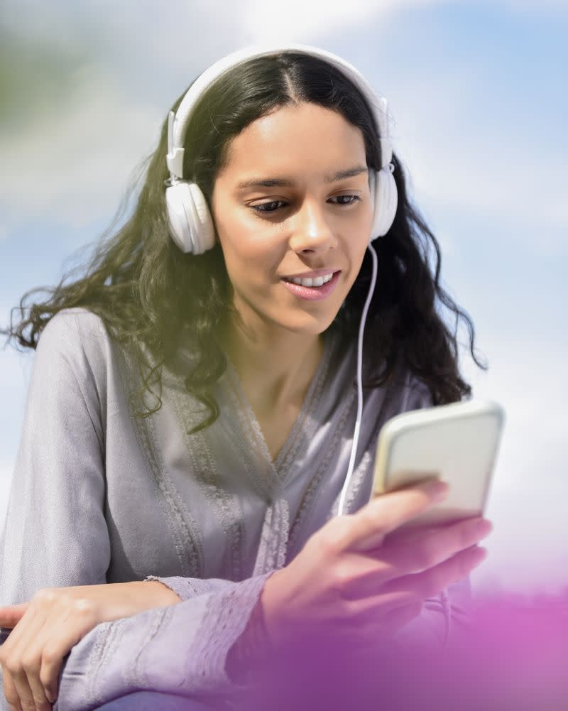 A woman wearing headphones looking at her phone screen