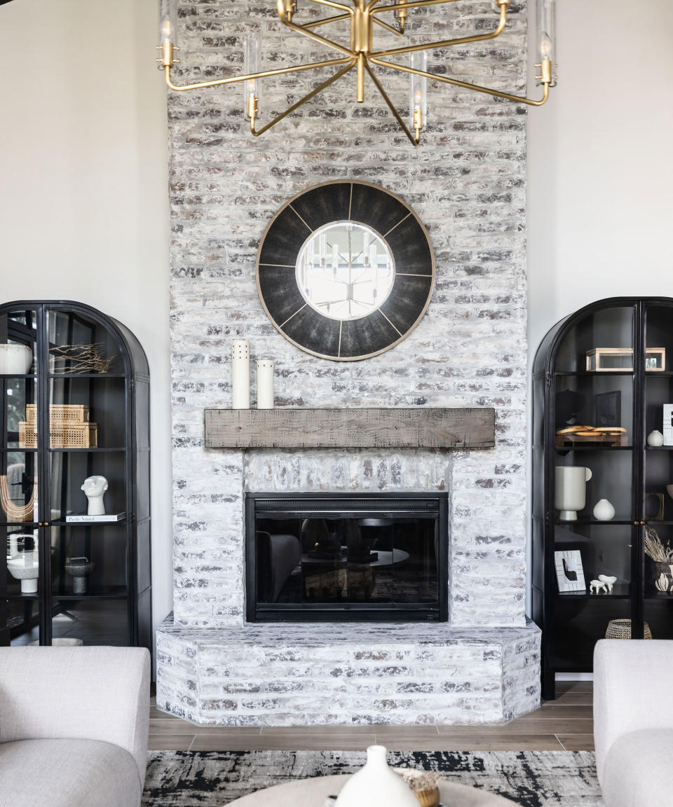 Round antique mirror with black trim above stone mantel in living room, with modern black bookcases either side