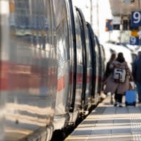 Reisende gehen mit Gepäck am Bahnsteig am Nürnberger Hauptbahnhof neben einem ICE entlang.