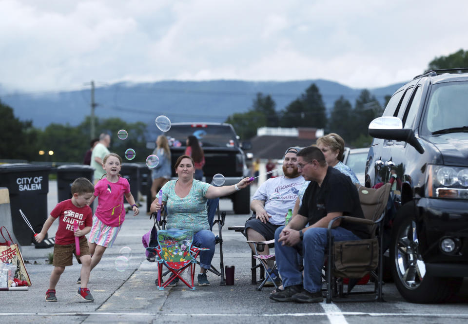 Alice Carr, 7, and her bother Bruce Carr, 3, chase bubbles being made by their mom, Olivia Carr, with their dad, Brandon Carr, and grandparents Rhonda and Eric Carr during a drive-in concert with Crawford & Power in the Salem Civic Center parking lot Thursday, June 18, 2020, in Salem, Va., amid the coronavirus pandemic. (Heather Rousseau/The Roanoke Times via AP)