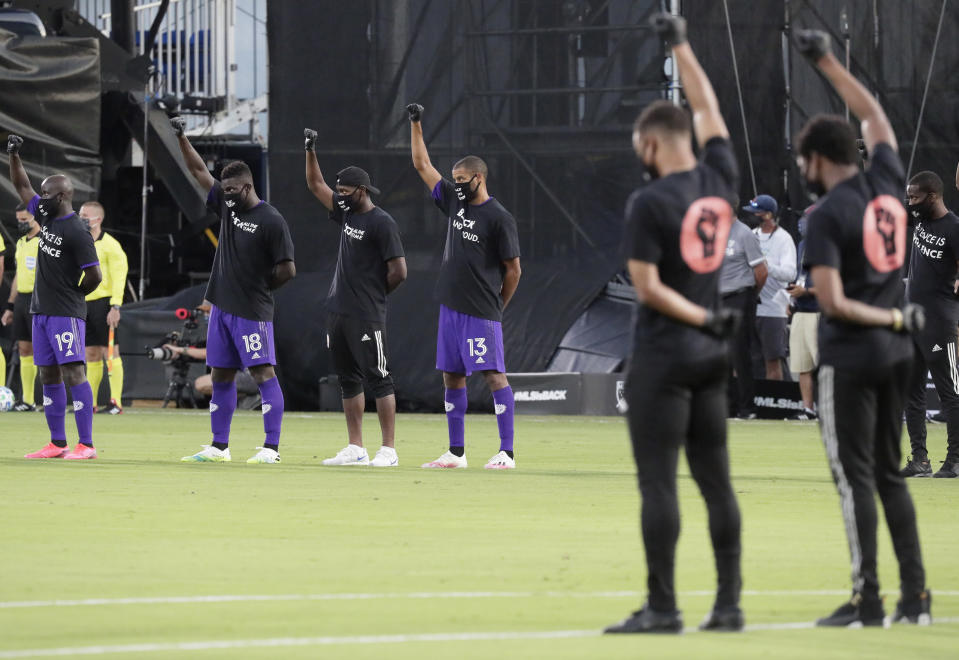 Orlando City players, left, raise their fists in the air in solidarity with other MLS teams before the start of an MLS soccer match, Wednesday, July 8, 2020, in Kissimmee, Fla., while wearing shirts and masks with messages about race. (AP Photo/John Raoux)