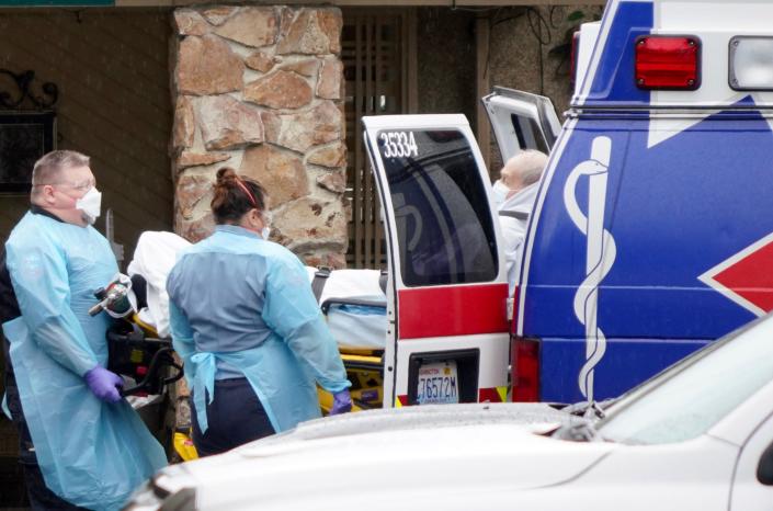 Medical workers load a sick patient into the back of a waiting ambulance for transport to a hospital from the Life Care Center of Kirkland, Washington, during the coronavirus outbreak.