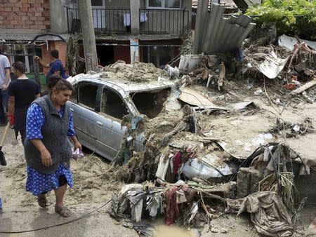 A woman walks past debris and a car destroyed by heavy floods in Varna June 21, 2014. REUTERS/Impact Press Group