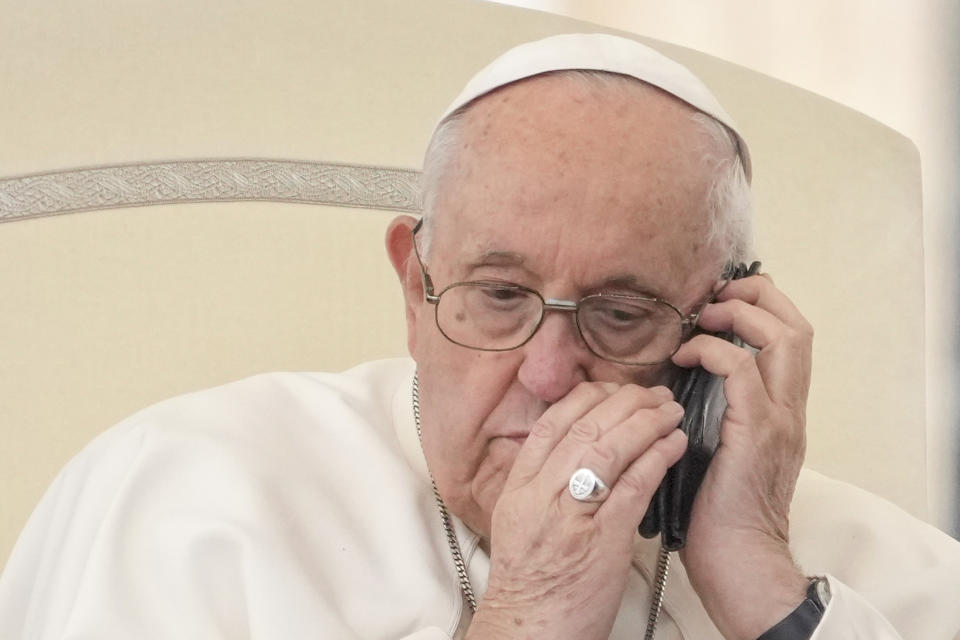 FILE-- Pope Francis talks on the phone during his weekly general audience in St. Peter's Square at the Vatican, Wednesday, May 17, 2023. During the period between the end of one pontificate and the election of a new pope the camerlengo, or chamberlain, runs the administration and finances of the Holy See, but under canon law Pope Francis was still pope, fully in charge of running the Vatican and the 1.3-billion-strong Catholic Church, even while unconscious and undergoing surgery Wednesday, June 7, 2023, to repair a hernia in his abdominal wall. (AP Photo/Andrew Medichini)