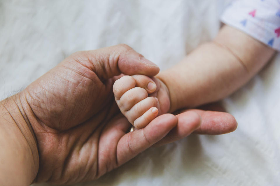 A close-up of a baby's hand gripping an adult's fingers, conveying a sense of connection and care