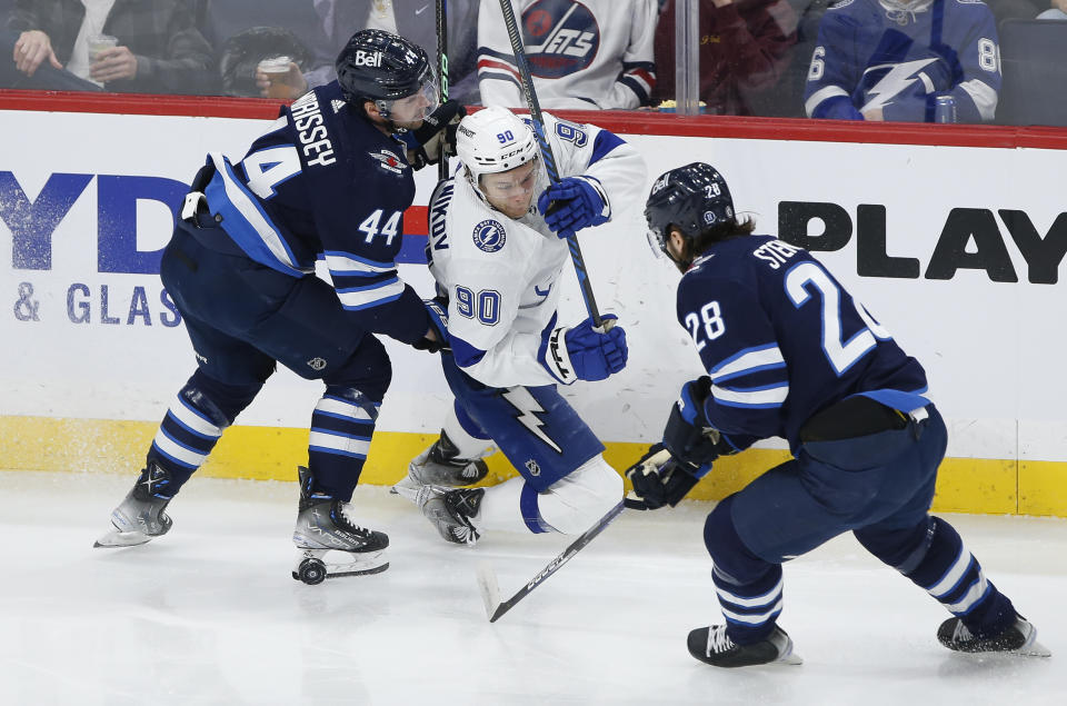 Winnipeg Jets' Josh Morrissey (44) defends against Tampa Bay Lightning's Vladislav Namestnikov (90) as Jets' Kevin Stenlund (28) picks ups the puck during second-period NHL hockey game action in Winnipeg, Manitoba, Friday, Jan. 6, 2023. (John Woods/The Canadian Press via AP)