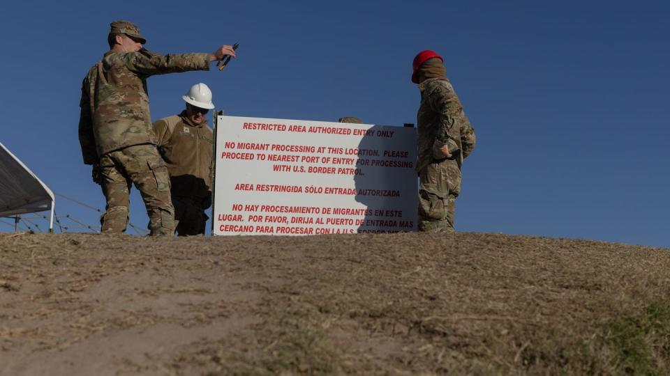 Texas National Guard members install a sign, meant to detract migrants from crossing the Rio Grande, at the bank of the river in Eagle Pass, on Jan. 17, 2024. (Eddie Gaspar/The Texas Tribune)